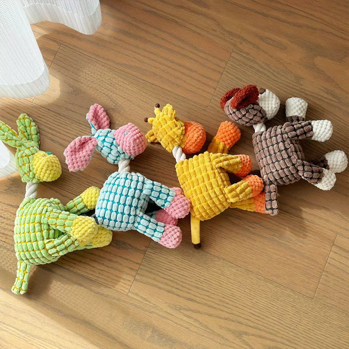 A collection of squeaky donkey plush toys in various colors and textures lying on a wooden floor.