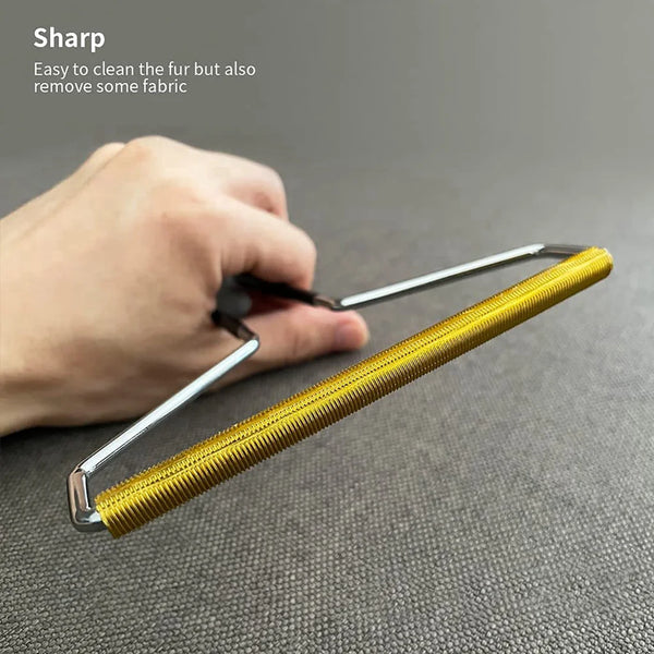 A hand is holding a yellow manual lint remover brush with a silver handle, demonstrating its use for removing fabric and pet 