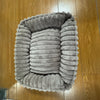 Un lit d'animal en peluche gris pour chiens et chats posé sur un plancher en bois.