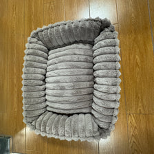 A gray plush pet bed designed for dogs and cats placed on a wooden floor.