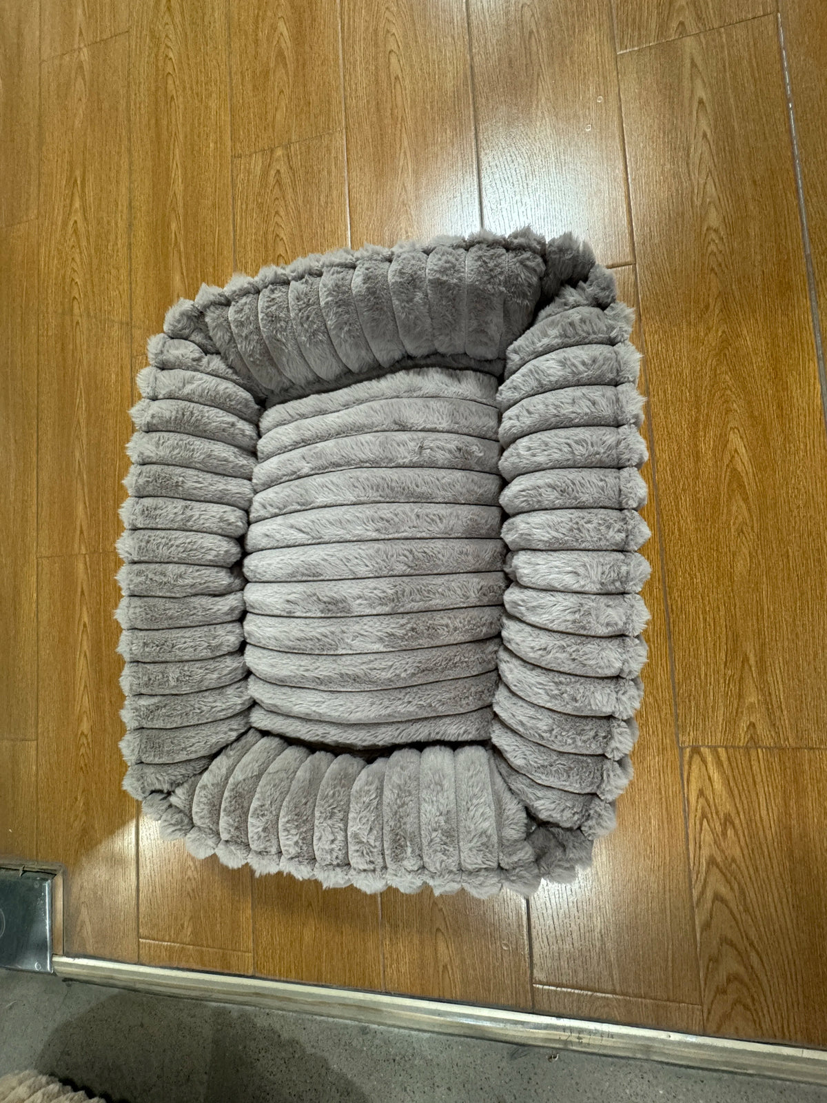 Un lit d'animal en peluche gris pour chiens et chats posé sur un plancher en bois.