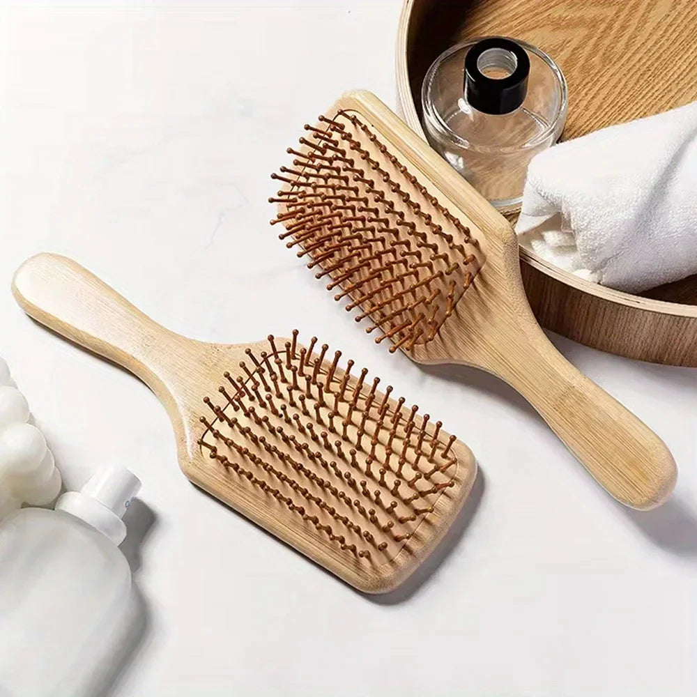 A wooden bamboo hair brush with massage bristles is shown next to a wooden bowl and a white towel.