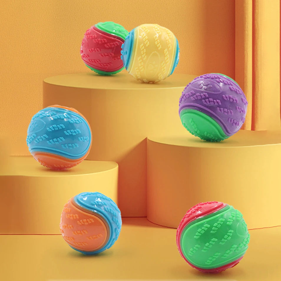 Eine Sammlung farbenfroher, strukturierter Hundeball-Spielzeuge in rosa, grün, gelb und blau auf einer hellorange Oberfläche.