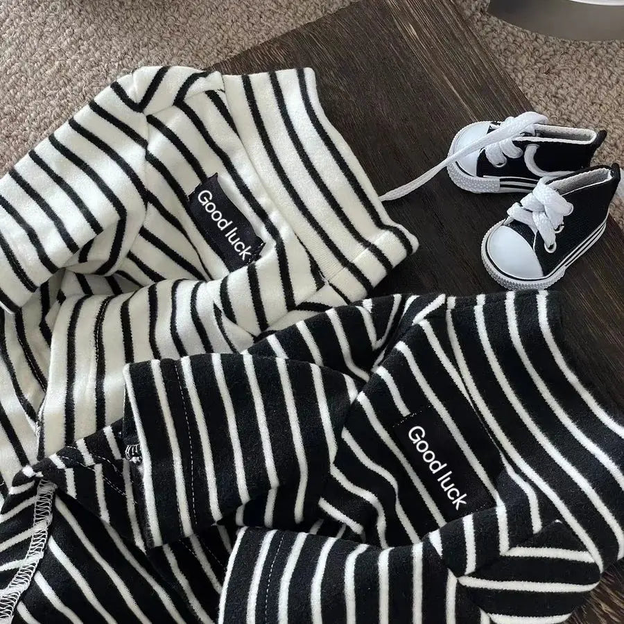 Black and white striped thermal dog sweater with a 'Good luck' logo lying on a wooden surface.