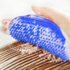 A close-up of a blue soft rubber pet grooming brush being used on a dog's fur.