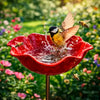 A red bowl bird feeder filled with water attracting bees in a garden setting.
