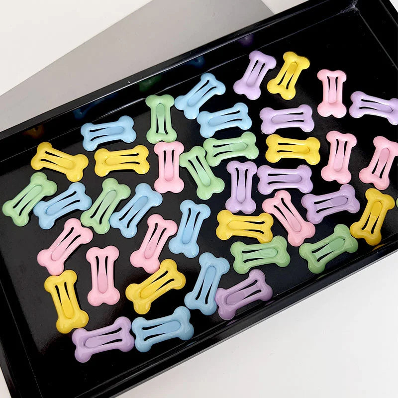 A collection of bone-shaped hair clips for pet grooming in various pastel colors arranged in a black tray.