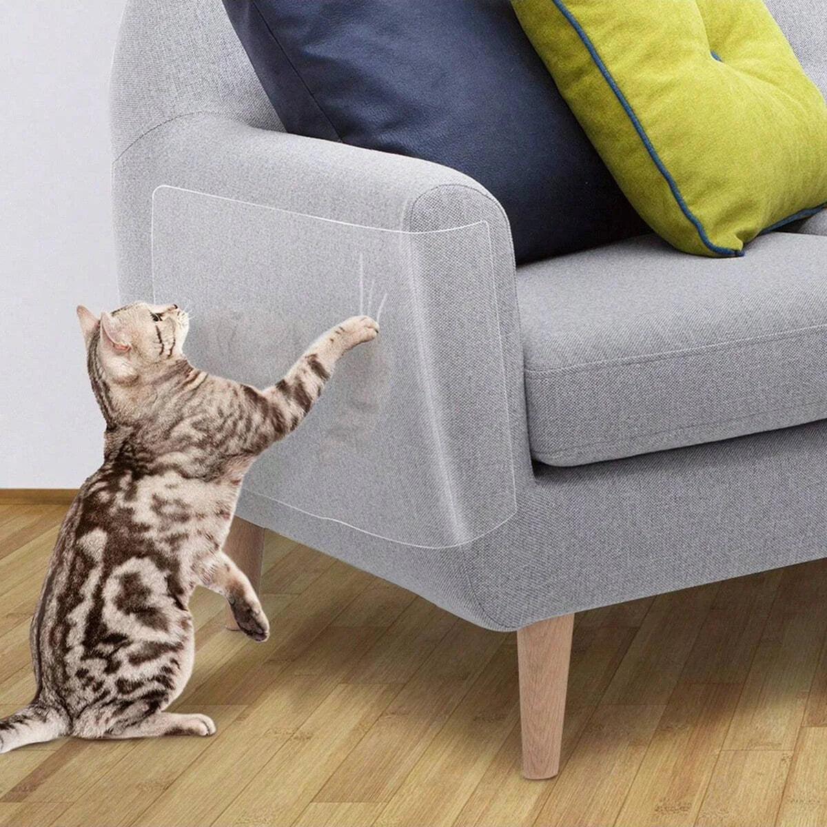 Eine tabbykatztiger sitzt auf einem grauen Sofa neben einem gelben Kissen.