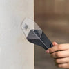 A hand holds a clear and black portable handheld insect catcher against a light-colored wall.
