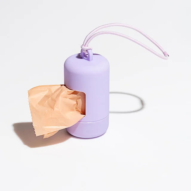 A purple portable dog poop bag dispenser with a pink strap is shown next to a crumpled piece of paper.