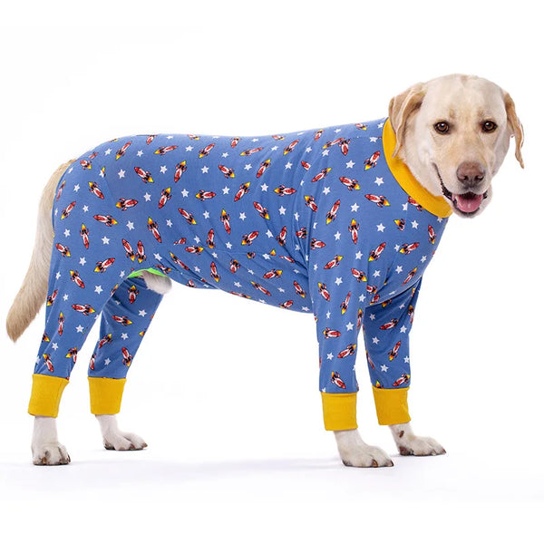 A light-colored dog wearing a blue jumpsuit covered in colorful cartoon animal prints.