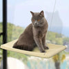 A gray cat is resting on a beige hammock bed suspended by strings in an outdoor setting.