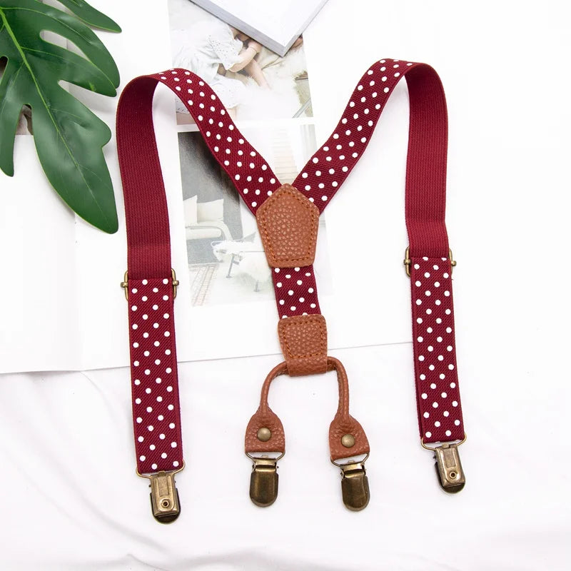 A pair of maroon suspenders with white polka dots and brown leather accents displayed on a white background.