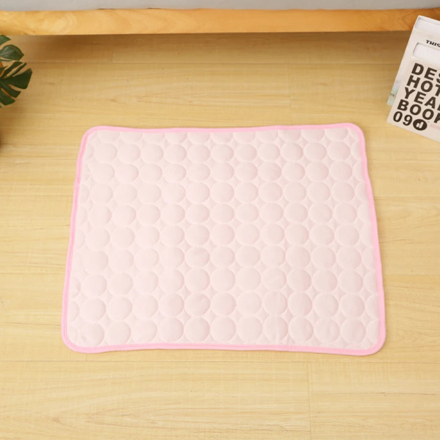 A pink quilted cooling mat designed for pet beds, placed on a light wooden surface.