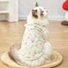 A fluffy white cat wearing a light-colored cotton dog vest with a lace collar and a floral cartoon print.