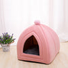 A pink cozy cat bed cave with a rounded shape and a fluffy pom-pom on top.