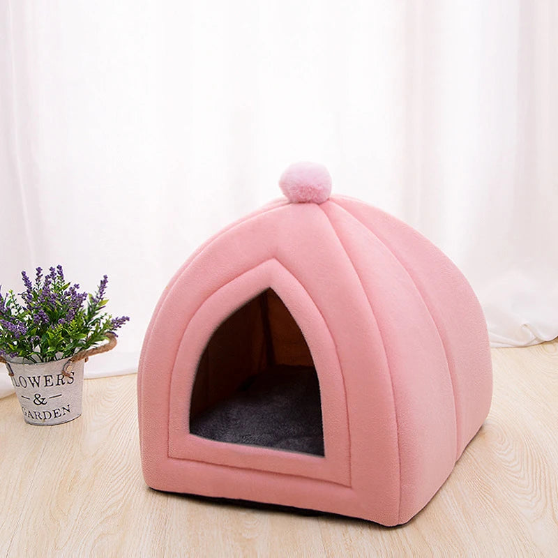 A pink cozy cat bed cave with a rounded shape and a fluffy pom-pom on top.