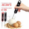 A hand holds a digital meat thermometer measuring the temperature of liquid in a glass, with raw eggs and wheat stalks nearby