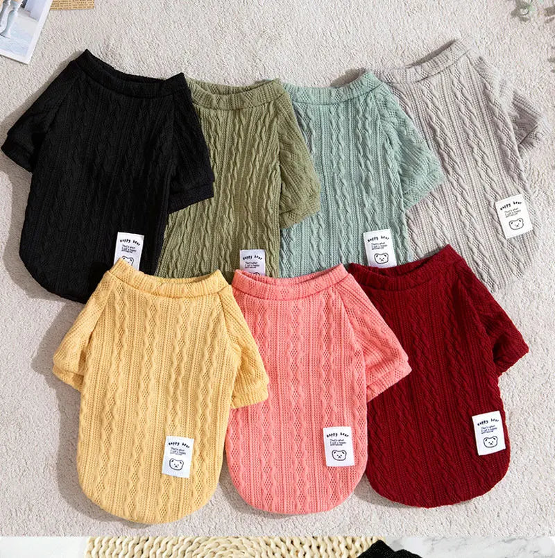 A collection of knitted winter sweaters for dogs and cats in various shades of green, yellow, pink, and red.