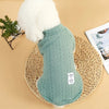 A light mint green knitted winter sweater for dogs or cats with a fluffy white collar, resting on a woven mat.