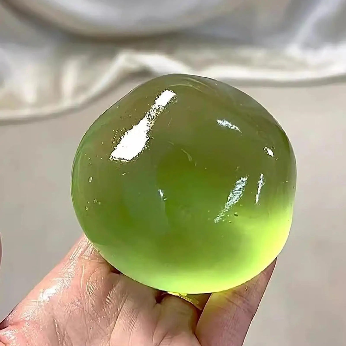 Eine Hand hält eine durchscheinende limettengrüne Stressball-Kugel vor einem hellen Hintergrund.