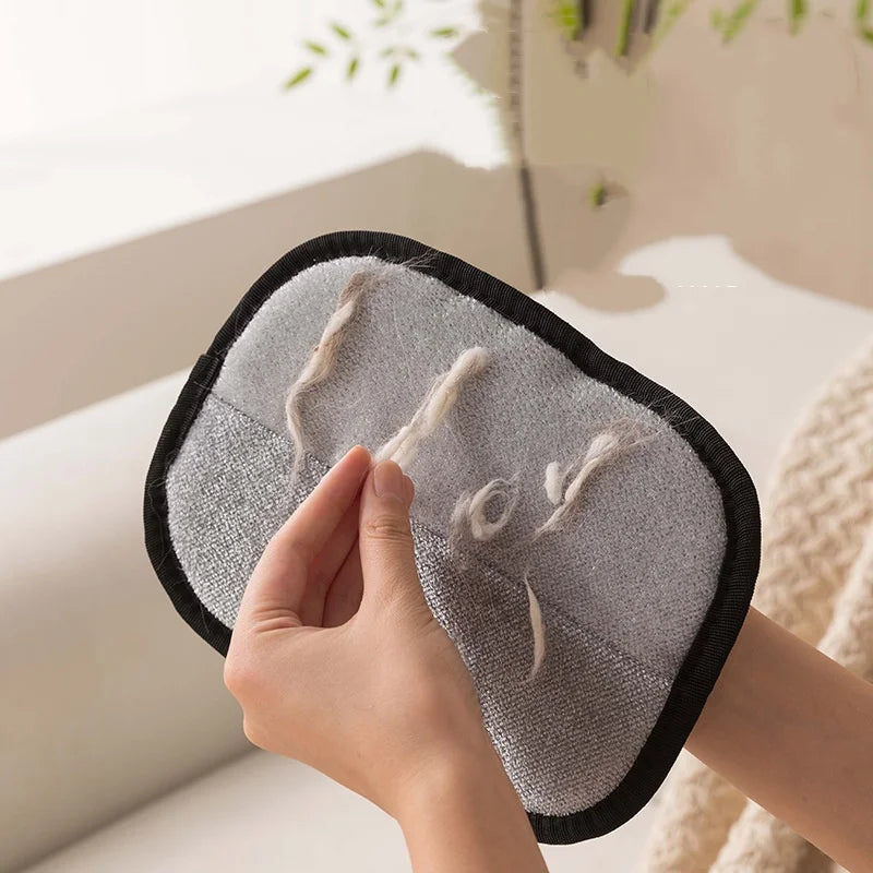 A hand is holding a pet hair removal glove for dogs and cats, showing the soft gray fabric and black trim.