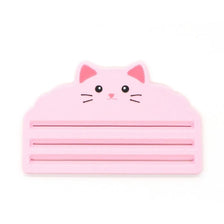 A pink reusable cat food pouch scraper shaped like a cat's head.