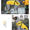A dog wearing a yellow and grey reflective waterproof raincoat with a hood standing in the rain.