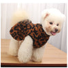 A fluffy white dog wearing a leopard print princess dress sitting on a wooden surface.