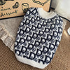A white and navy knit sweater for dogs with a repeating diamond pattern, displayed on a brown surface.