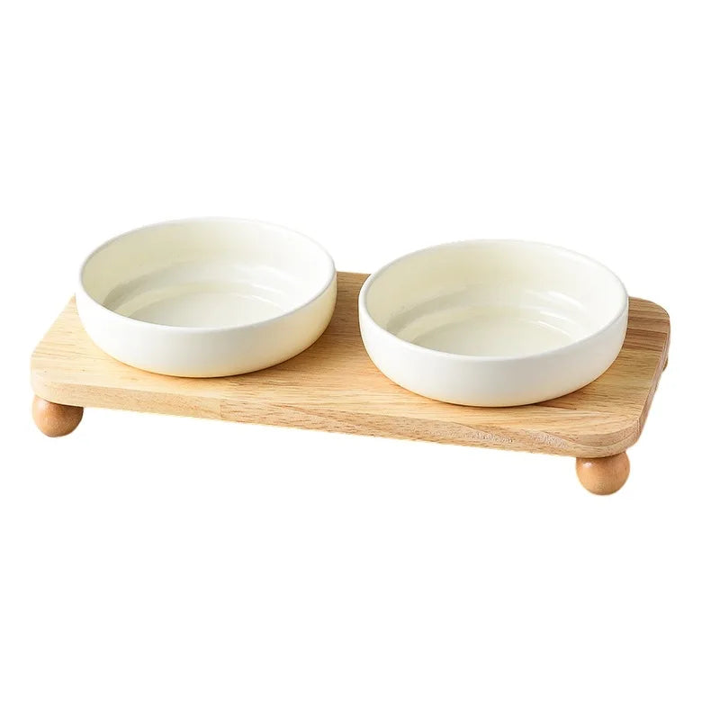 A pair of white ceramic cat and dog bowls resting on a light wooden stand.