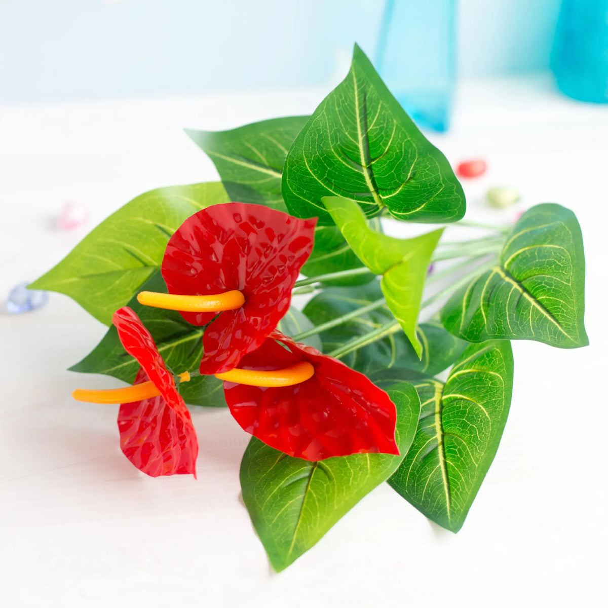 Fausse plante d'anthurioème rouge vif avec des feuilles vertes et des spathes jaunes sur une surface blanche.