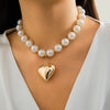 A close-up of a pearl choker necklace with a heart pendant worn against a light-colored garment.