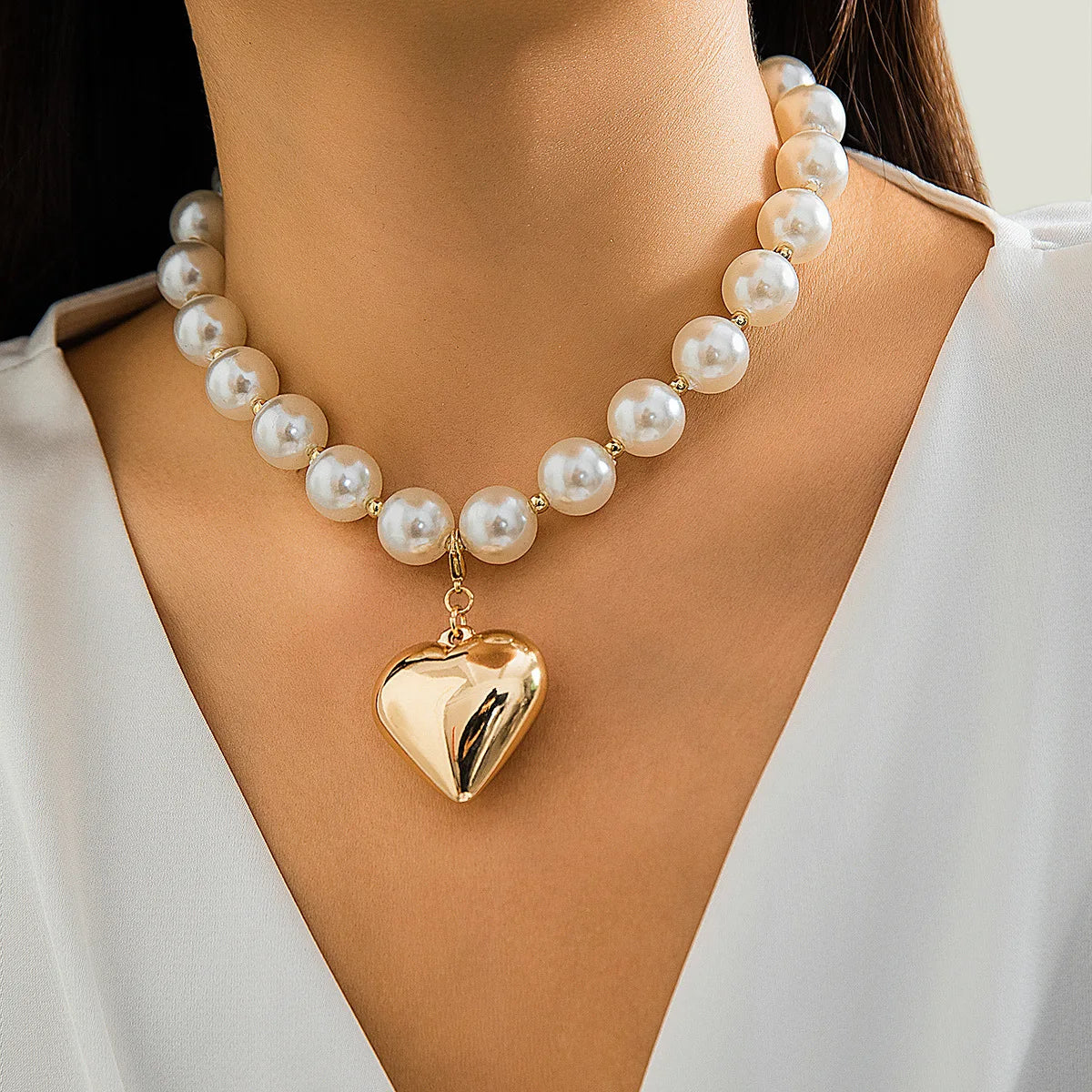 A close-up of a pearl choker necklace with a heart pendant worn against a light-colored garment.