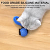 A gray cat is interacting with a blue silicone cat toy on a wooden surface.