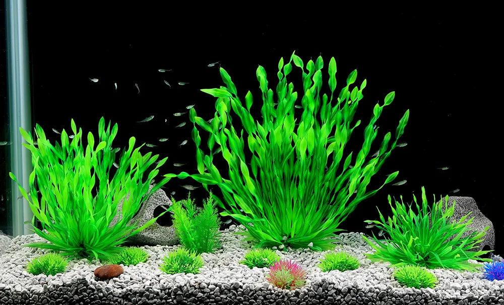 A vibrant display of artificial aquatic plants in various shades of green and pink growing on a light gravel substrate.