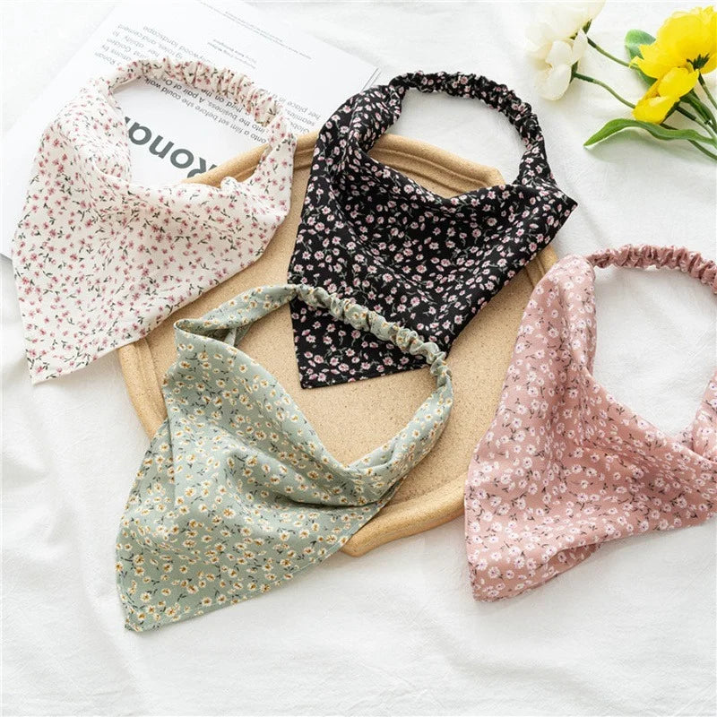 Three patterned fabric head scarves, including floral and dark print designs, are displayed on a white surface.