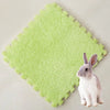 A small gray rabbit sits on a bright lime green, fluffy fleece pet warming mat.