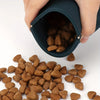 A hand is holding a dark silicone pouch filled with brown dog treats.