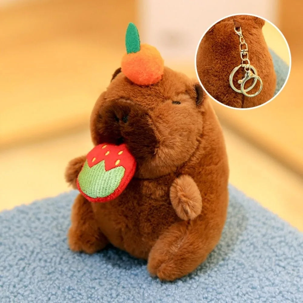A brown capybara plush toy with an orange flower on its head and a green leaf attached to its mouth.