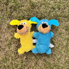 Two plush dog toys, one yellow and one blue, lying on green grass.