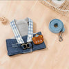 A blue and white plaid dog harness vest with a brown cartoon dog charm and attached leash.