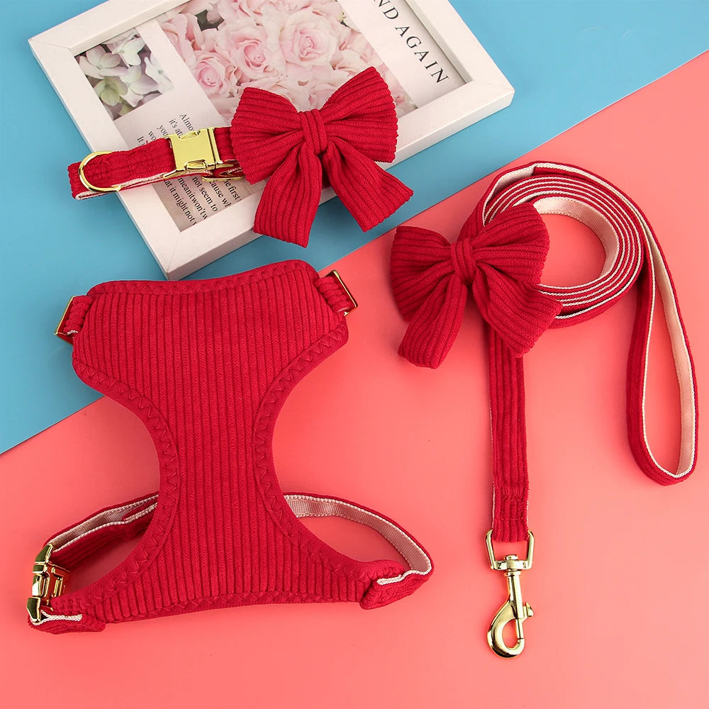 A red knitted dog harness, collar, and leash set with a large bowknot displayed on a pink background.