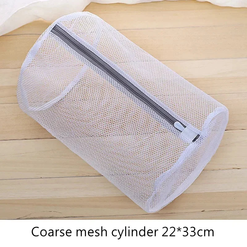 Bolsa de ropa cilíndrica de malla clara con cremallera, tumbada sobre una superficie de madera.