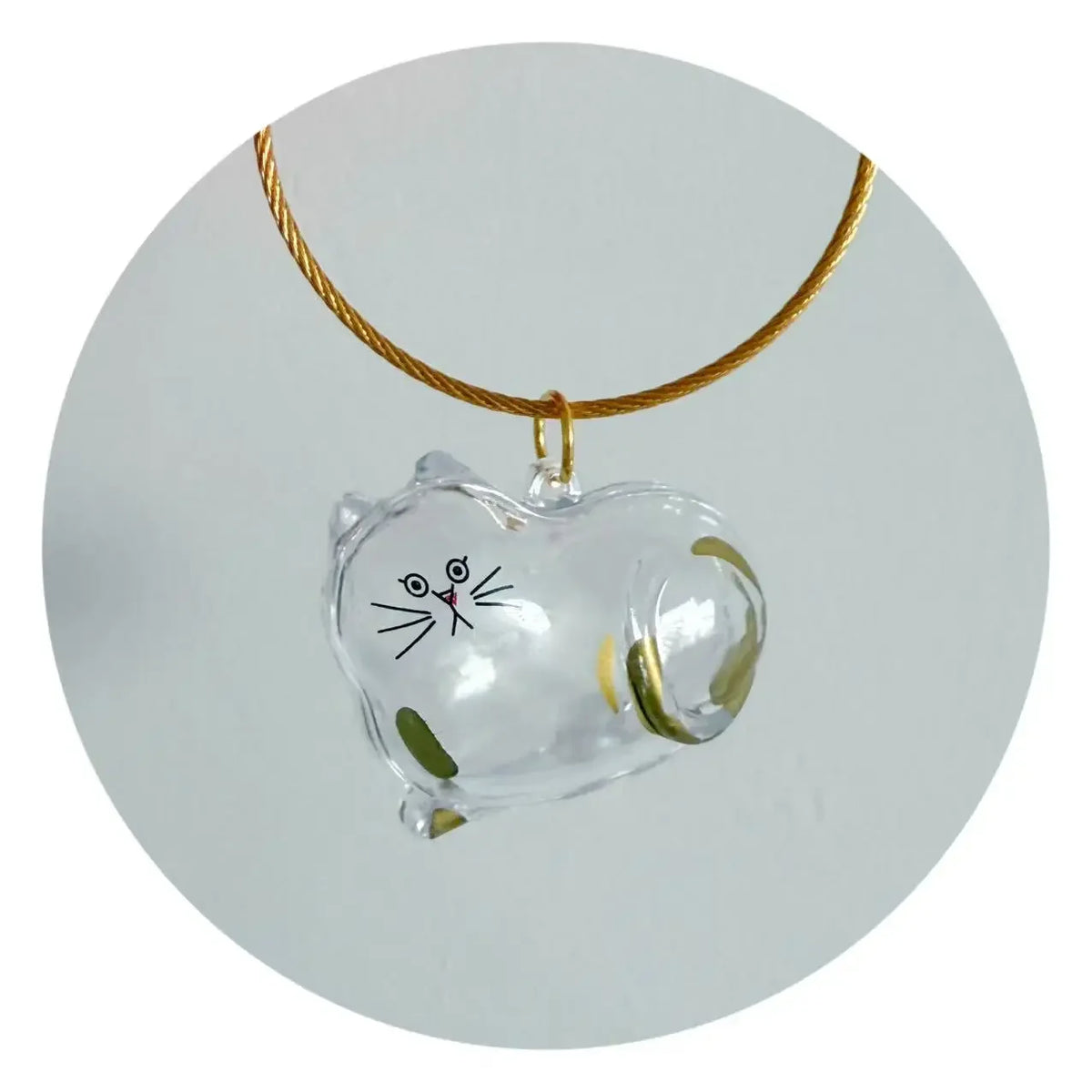 Un charm en verre transparent en forme de chat suspendu à une corde dorée.