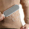 Una mano sostiene un dispositivo de quitapelusas de silicona gris contra un suéter de punto beige.