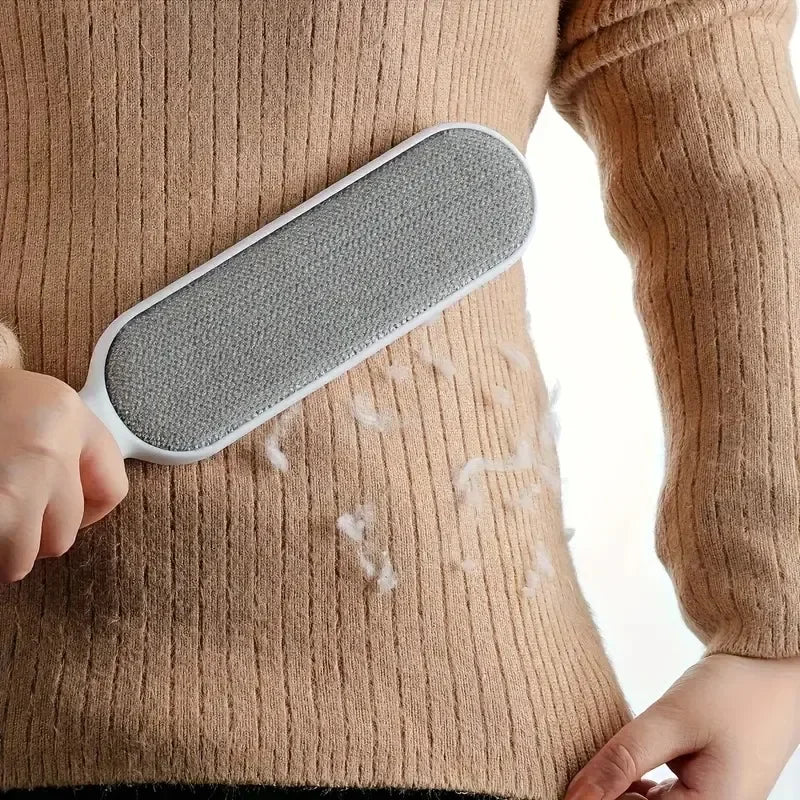 Una mano sostiene un dispositivo de quitapelusas de silicona gris contra un suéter de punto beige.