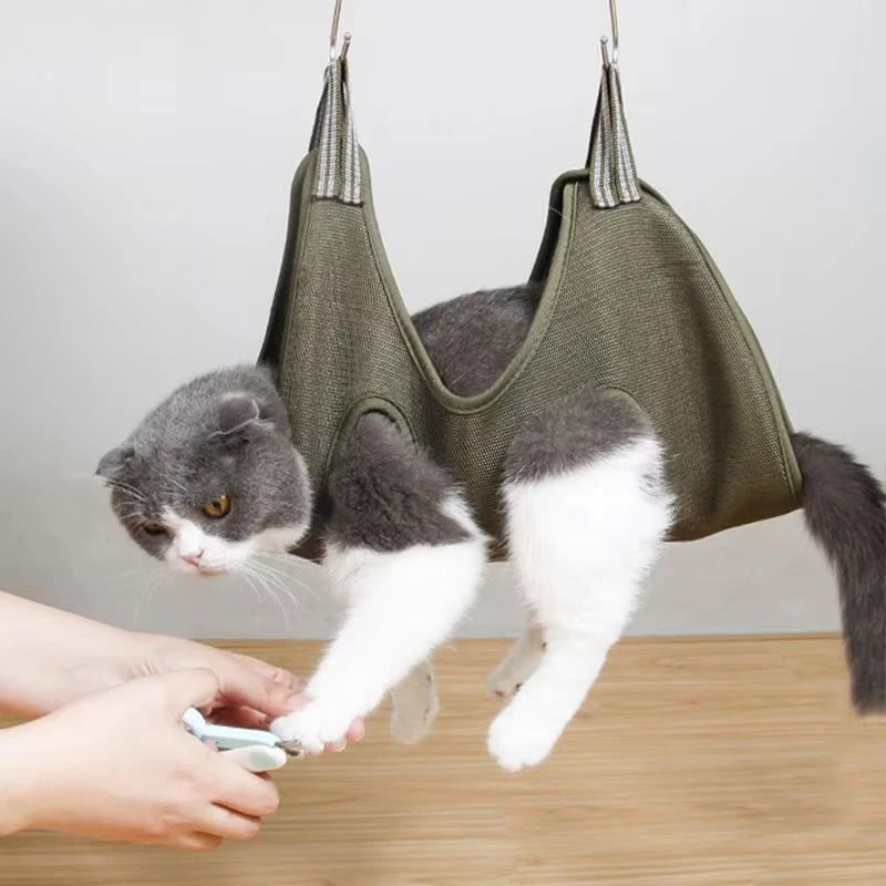 Un chat se repose dans une hamac de toilettage verte pendant qu'une personne utilise un outil sur sa patte.