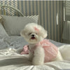 A fluffy white dog wearing a pink tulle dress lying on white bedding.