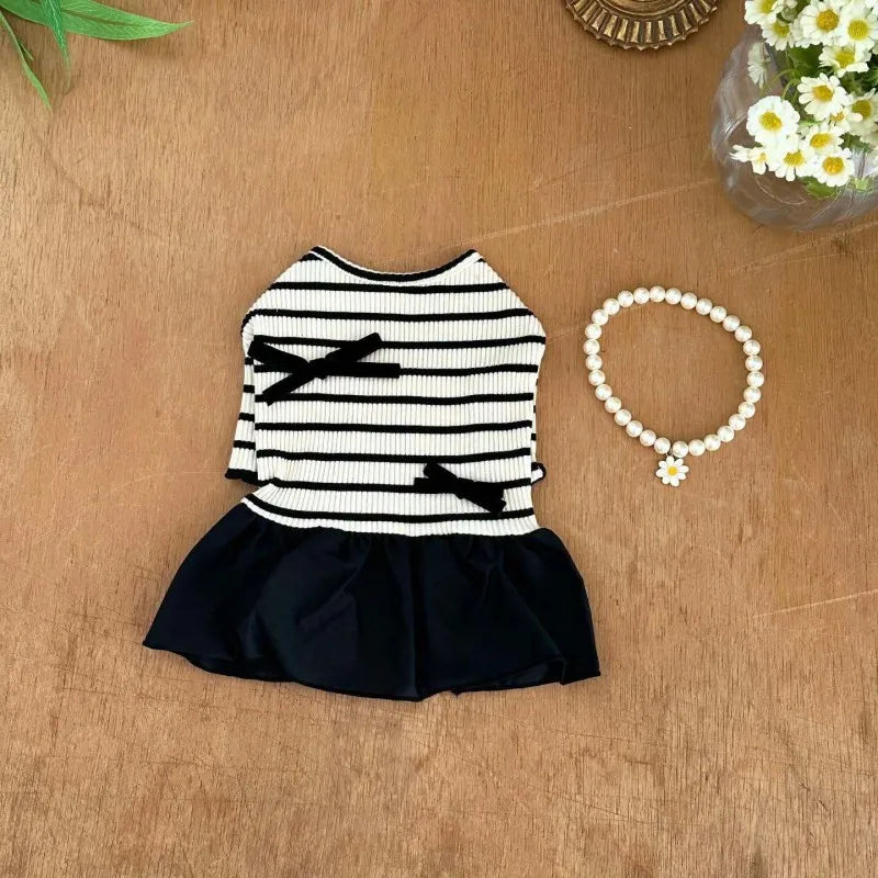 A black and white striped pet dress for a small dog with a ruffled skirt, placed on a wooden surface.